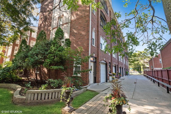 Front view of a multi-story brick building with gardens and garages.
