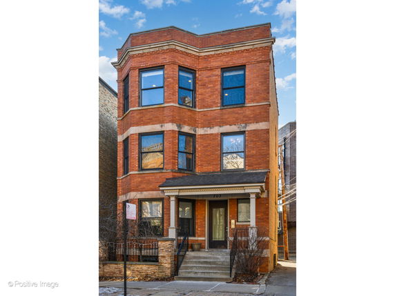 Front view of a three-story brick building with multiple windows and a small entrance porch.