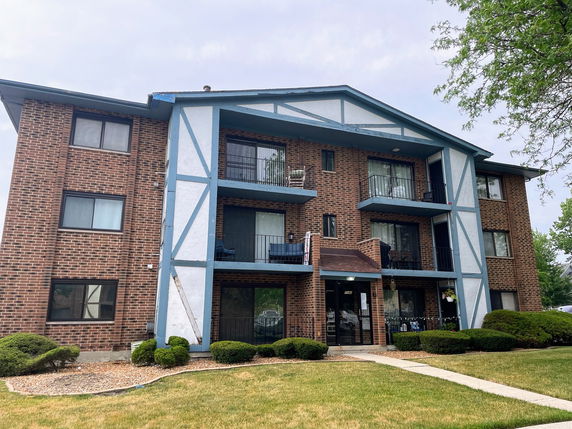 Front view of a brick multi-story apartment building with balconies.