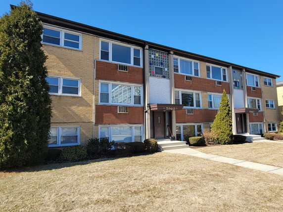 Front view of a three-story apartment building with a mix of brick and decorative paneling.