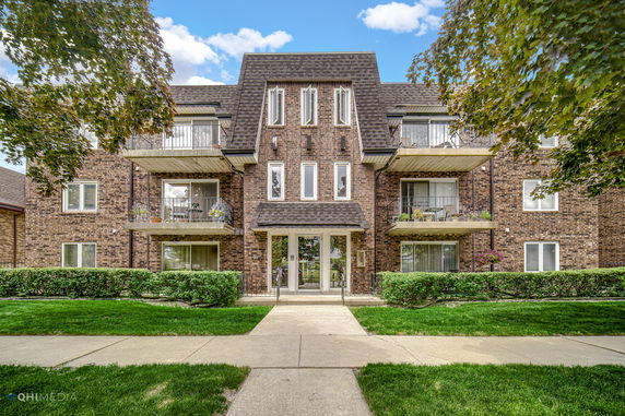 Front view of a three-story brick apartment building with balconies.