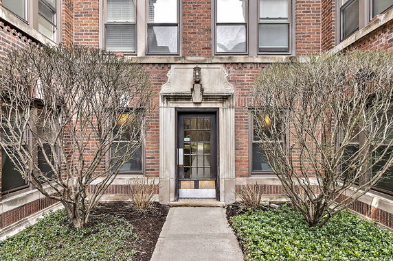 Front view of a brick building entrance with windows and trimmed shrubs.