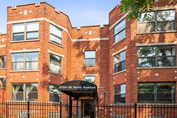 Front view of a brick apartment building with large windows and an entrance canopy.