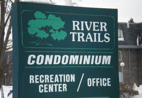 Sign for River Trails Condominium in front of a building.