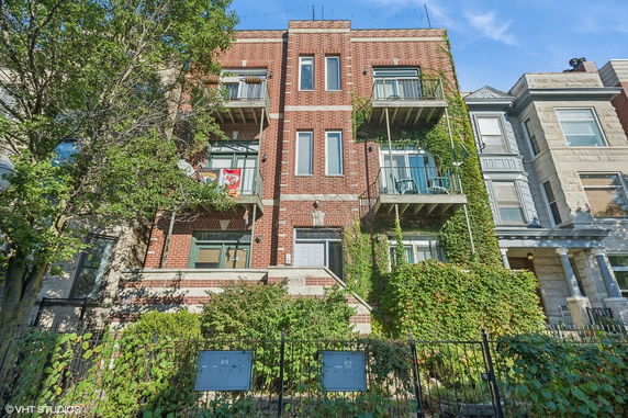 Front view of a three-story brick apartment building with balconies and ivy-covered facade.