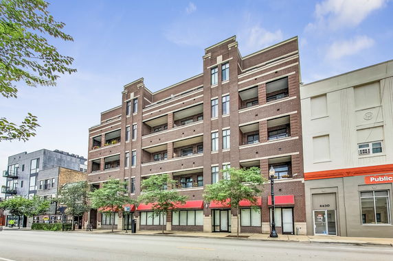 Front view of a multi-story brick building with balconies and red awnings.