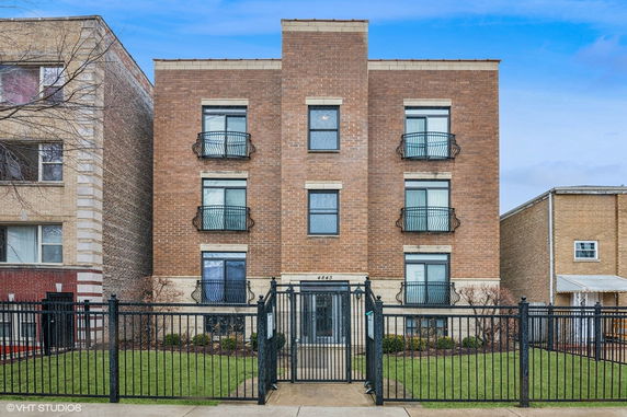 Front view of a three-story brick apartment building with metal railings on the windows.