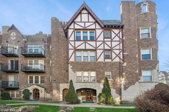 Front view of a brick residential building with multiple balconies and a decorative gable.