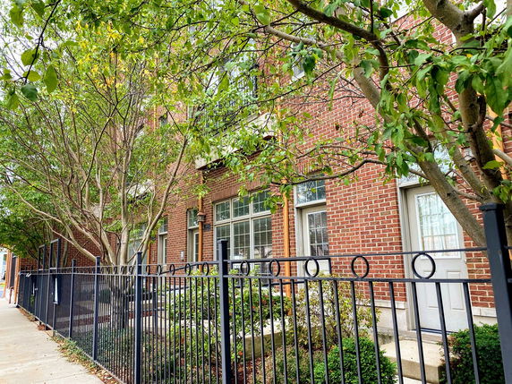 Front view of a brick residential building with large windows and a metal fence.