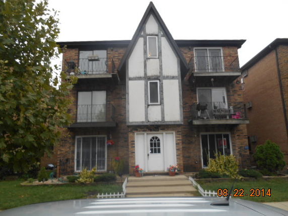 Front view of a three-story apartment building with a triangular roof and balconies.