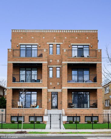 Front view of a brick multi-story residential building with balconies on each floor.