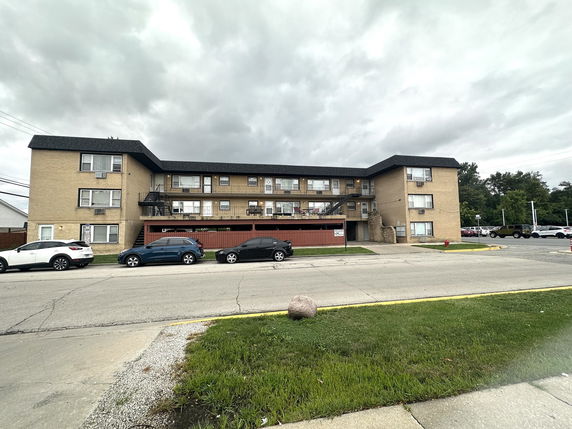 Front view of a three-story apartment building with parking spaces in front.