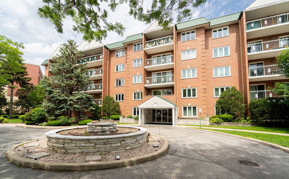 Front view of a multi-story residential building with balconies and a circular driveway.