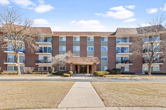 Front view of a multi-story brick apartment building with balconies and a covered entrance.