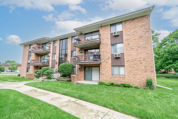 Front view of a three-story brick apartment building with balconies and air conditioning units.