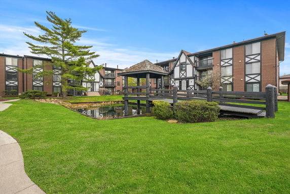 Front view of apartment buildings with a small pond and wooden gazebo in the foreground.
