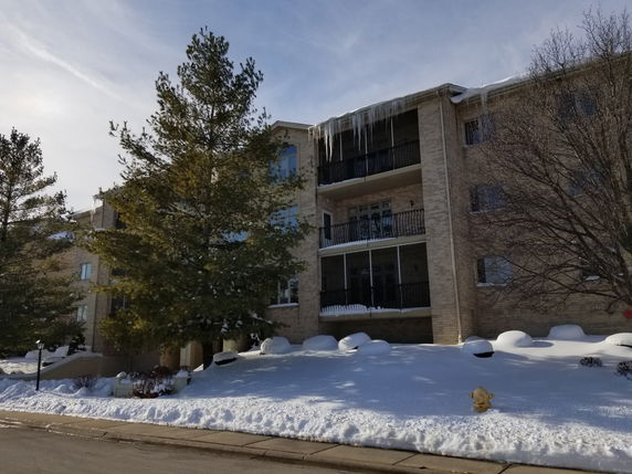 Front view of a multi-story residential building with balconies and icicles hanging from the roof.