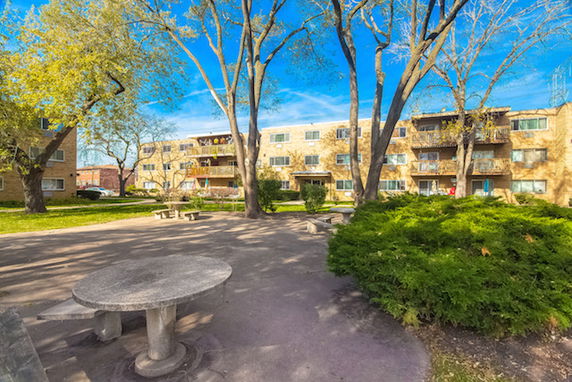 Outdoor view of apartment buildings with a central courtyard area surrounded by trees.