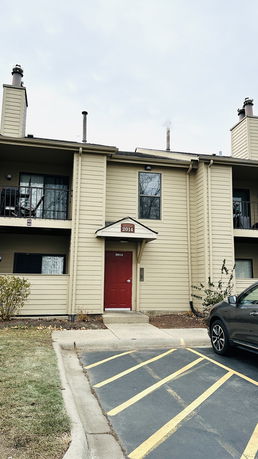 Front view of a two-story residential building with a red entrance door and balconies.