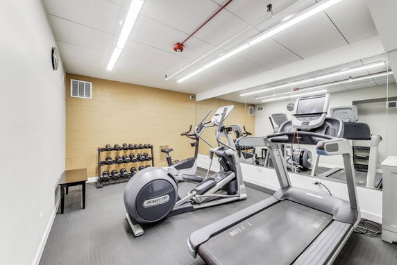 Room with gym equipment including treadmills and weights.