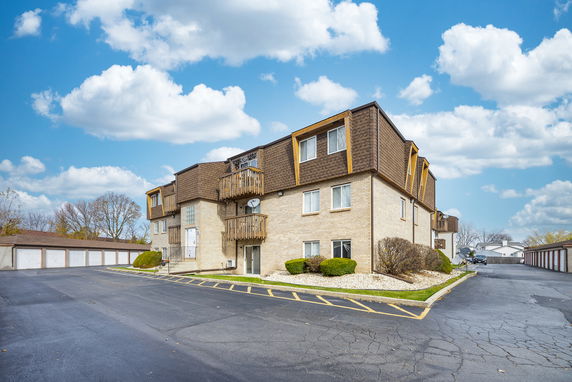 Front view of a multi-story apartment building with balconies and an asphalt driveway.