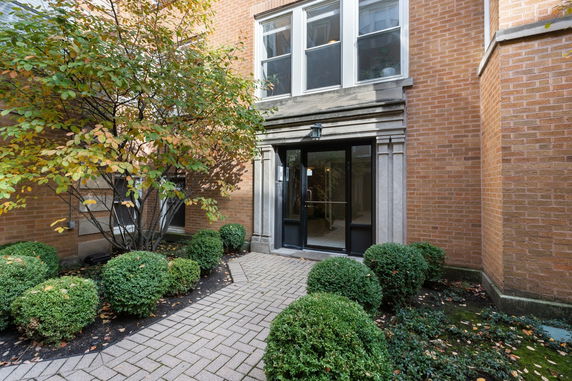 Front view of a brick building entrance with large windows above and surrounding greenery.