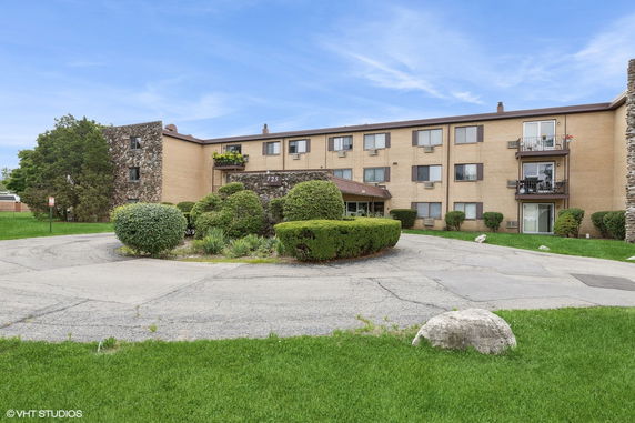 Front view of a three-story apartment building with balconies and surrounding greenery.