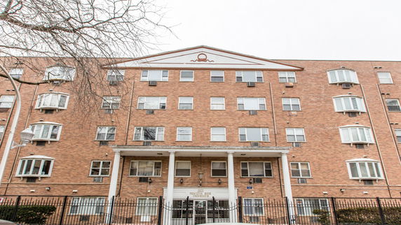 Front view of a multi-story brick building with rectangular windows and a gated entrance.