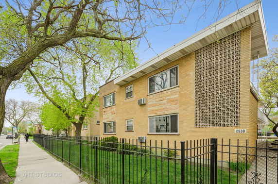 Front view of a two-story brick building with iron fencing and large windows.