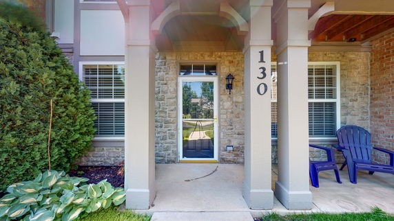 Front view of a house entrance with stone and brick facade, featuring a glass door and two windows.