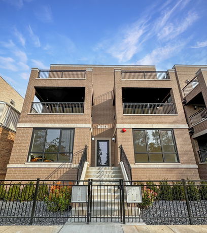 Front view of a three-story brick building with balconies and a central entrance staircase.