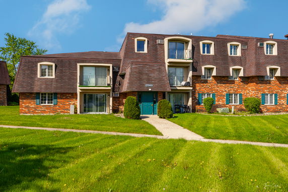 Front view of a multi-story apartment building with brown shingled roof and brick facade.