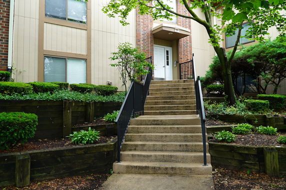 Front view of a building with a concrete staircase and a landscaped entrance.