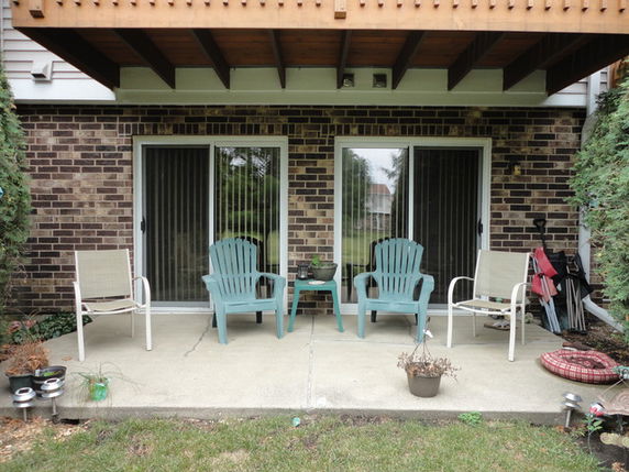 Front view of a house with sliding glass doors and a small patio area with chairs.
