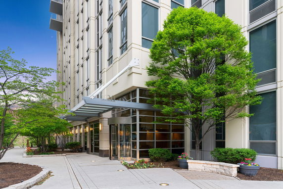 Front view of a modern multi-story building with glass entrance and surrounding greenery.