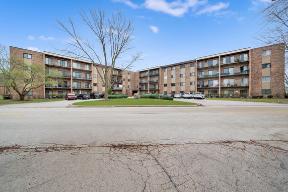 Front view of a multi-story apartment building with balconies and parking area.