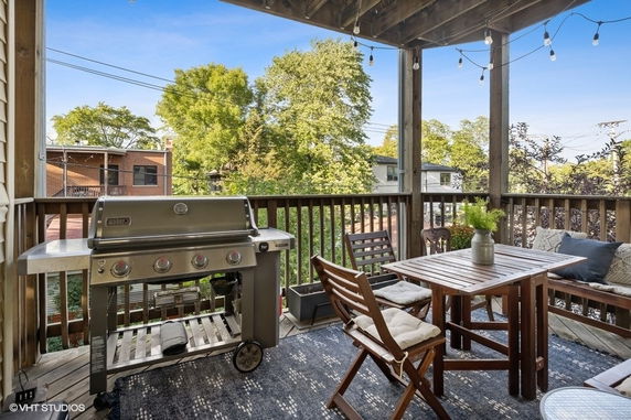 Rooftop area with a grill and wooden seating set, enclosed by railings.