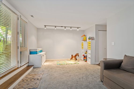 Room with carpeted floor, window blinds, couch, and children's toys.