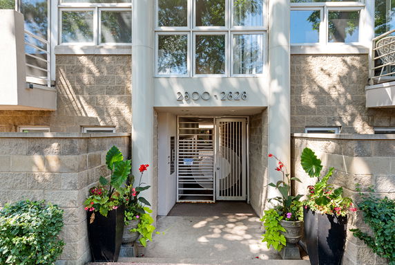 Front view of a building entrance with a metal gate and decorative plants.