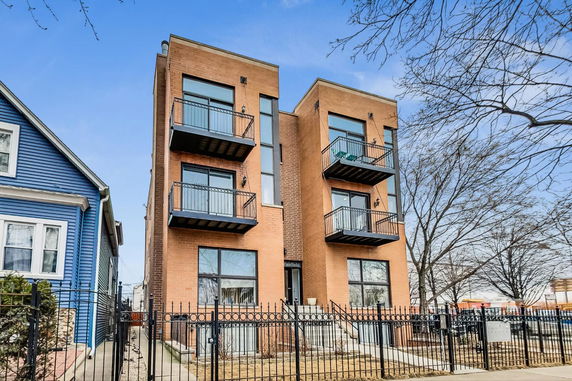 Front view of a modern three-story brick apartment building with balconies.