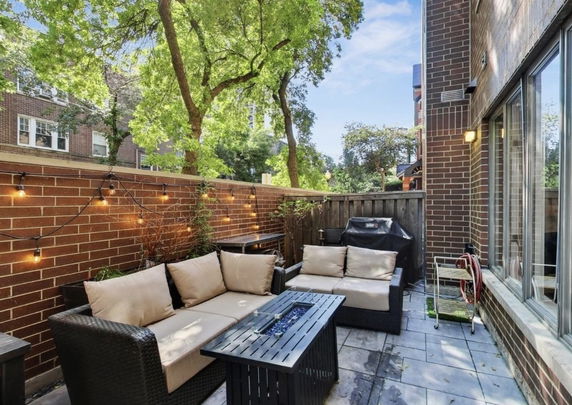 Outdoor patio area with seating and a grill, surrounded by brick walls and trees.