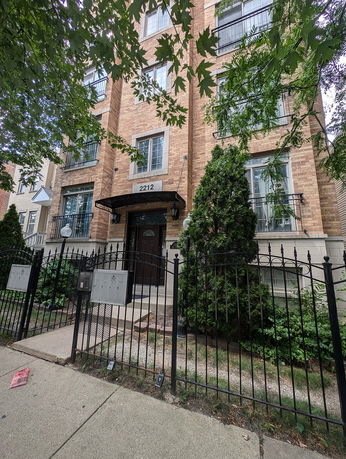 Front view of a multi-story brick building with a fenced entrance.