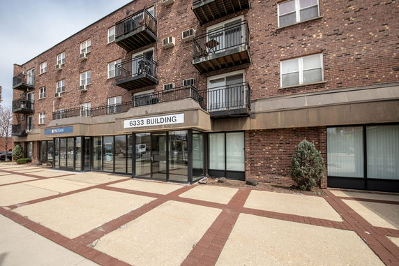 Front view of a multi-story brick building with balconies and glass entry doors.