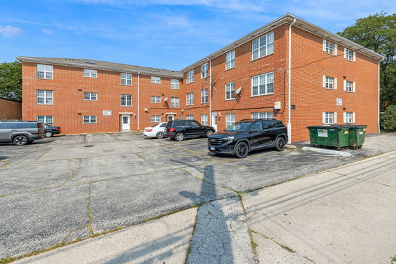 Front view of a three-story brick apartment building with parking area.