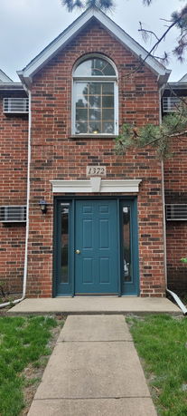 Front view of a two-story brick house with a blue door and arched window above.