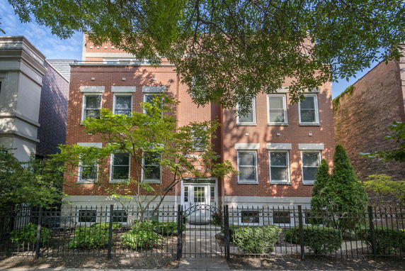 Front view of a three-story brick house with multiple windows and a small entrance gate.