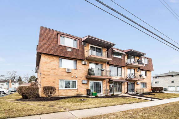 Front view of a three-story apartment building with balconies and brick facade.