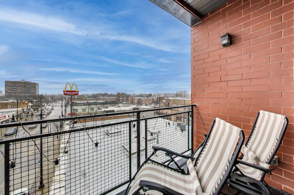 View from a balcony with two lounge chairs and a cityscape in the background.