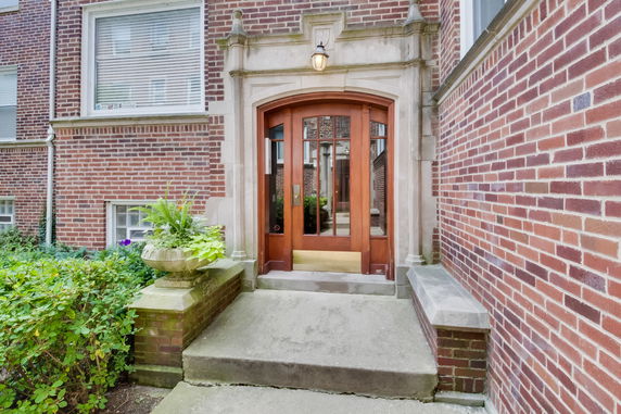 Front view of a brick building entrance with a wooden door and decorative stone frame.
