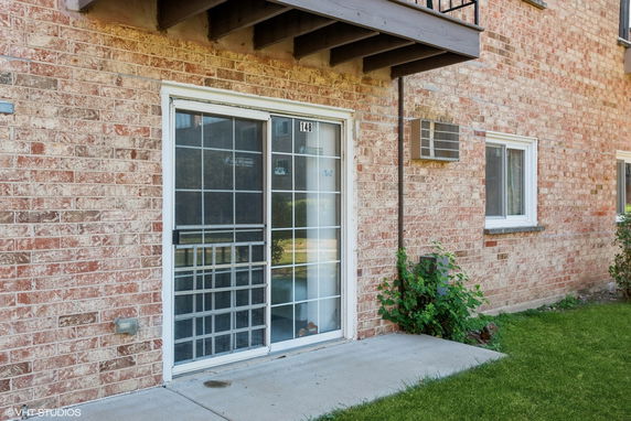 Close-up view of a brick building facade with a sliding glass door and a small window air conditioner unit.